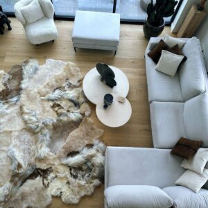 Melange patchwork schapenvacht tapijt in een woonkamer met eiken vloer, lichte zetel en bouclé fauteuil